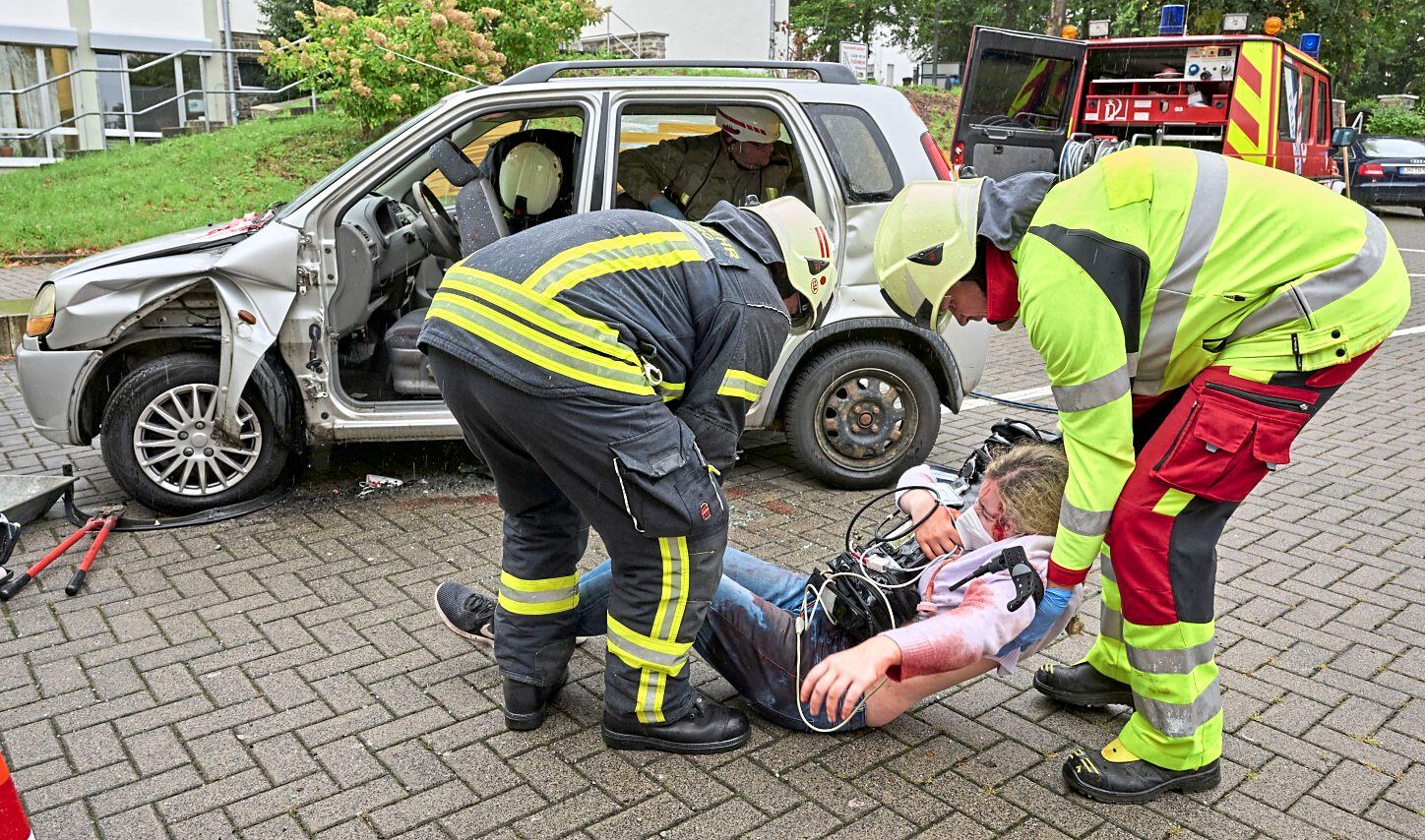 Gemeinsam mit einem Feuerwehrmann hebt Notarzt Benjamin Neeb (rechts) eine verletzte Person aus dem Unfallfahrzeug.